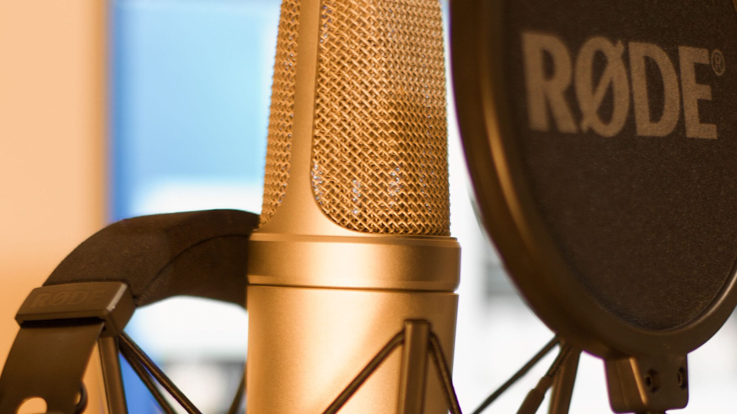 Close-up of a condenser microphone and headphones in a recording studio with soft lighting.